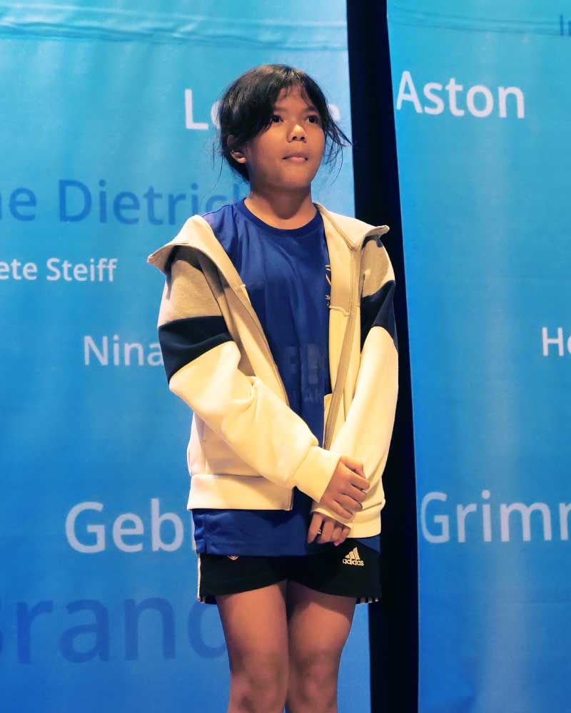 A young girl stands in front of a banner that says aston