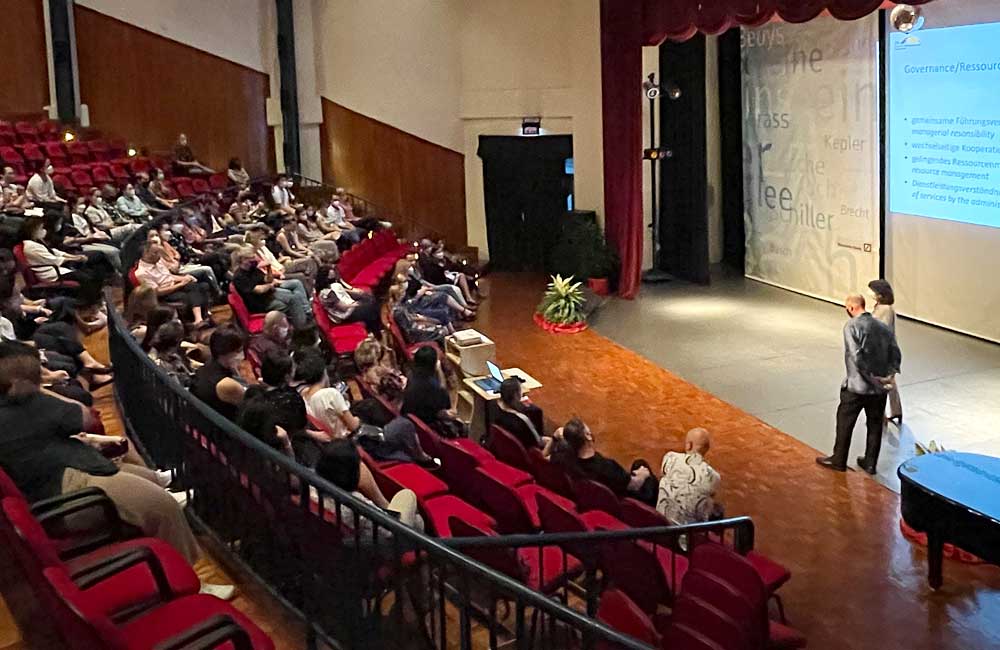 A large group of people are sitting in an auditorium watching a presentation.