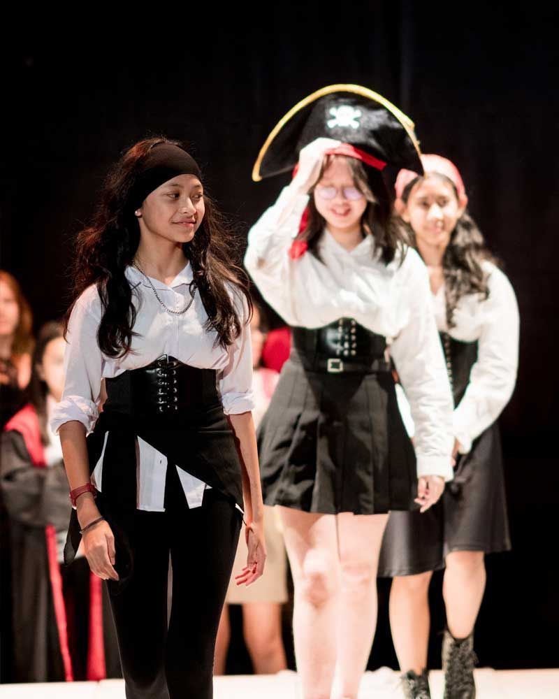 A group of girls dressed in pirate costumes are walking on a stage.