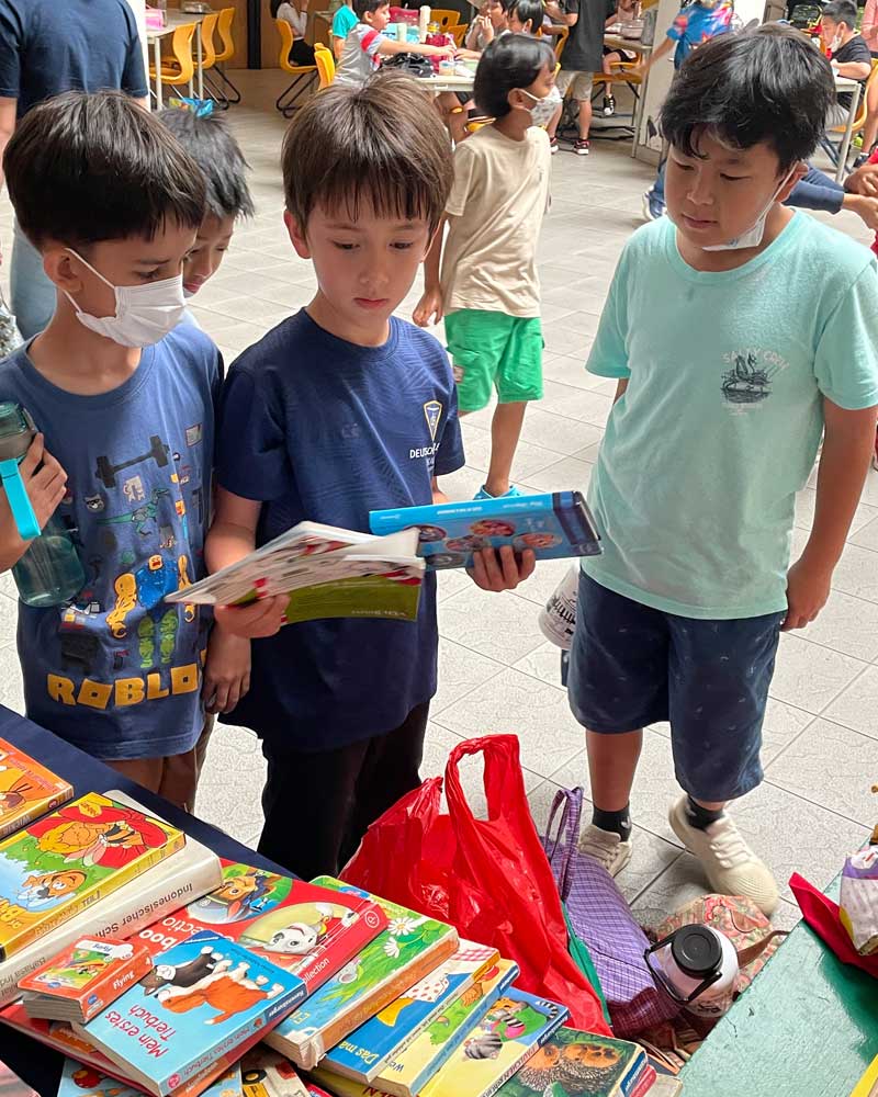 A group of young boys are standing around a table looking at books.