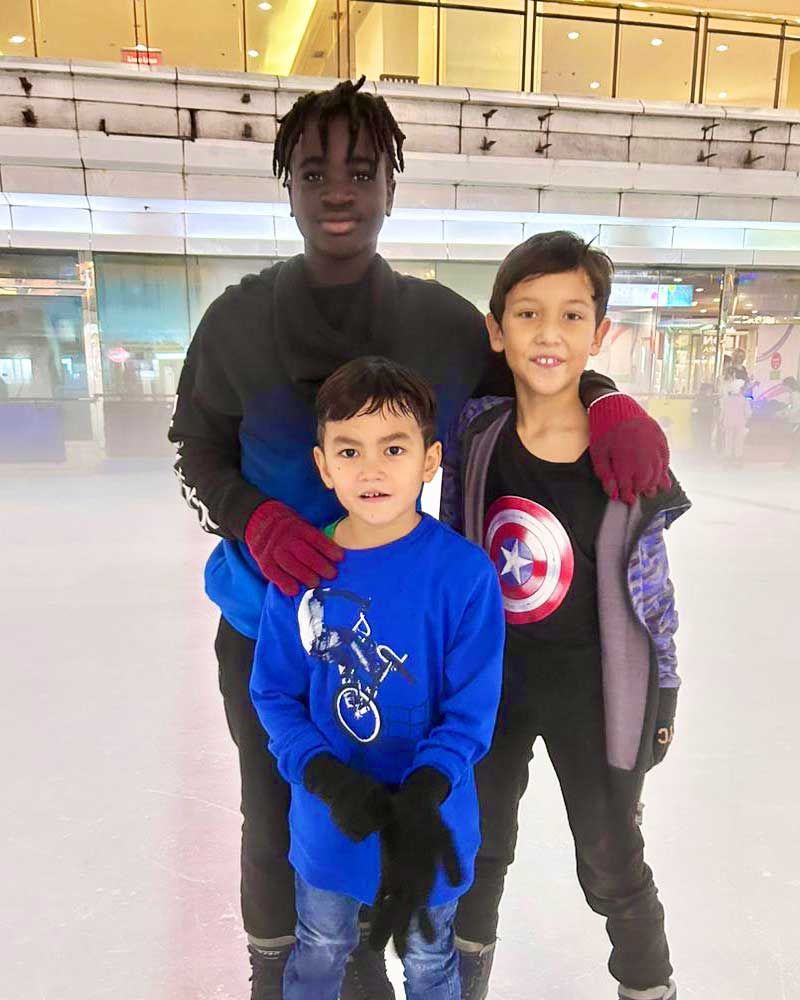 A man is standing next to two young boys on a ice rink.