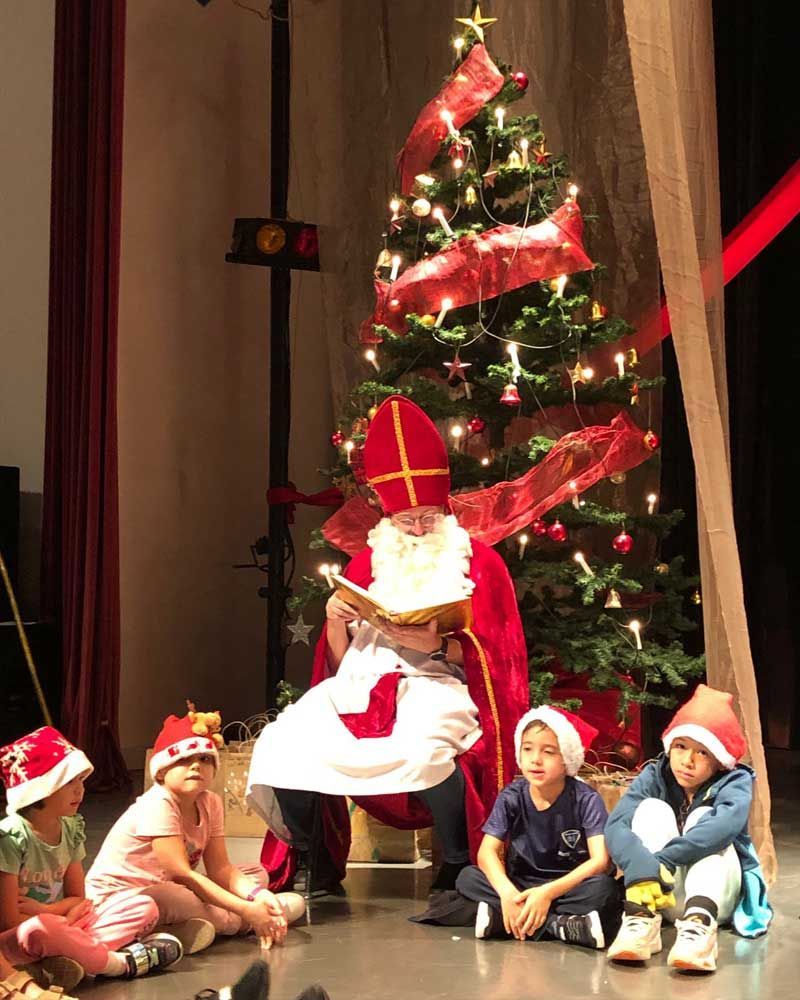 A group of children are sitting on the floor in front of a christmas tree.