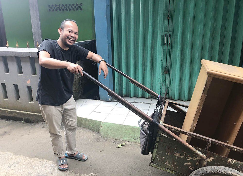 A man is pushing a cart with a piece of furniture in it.