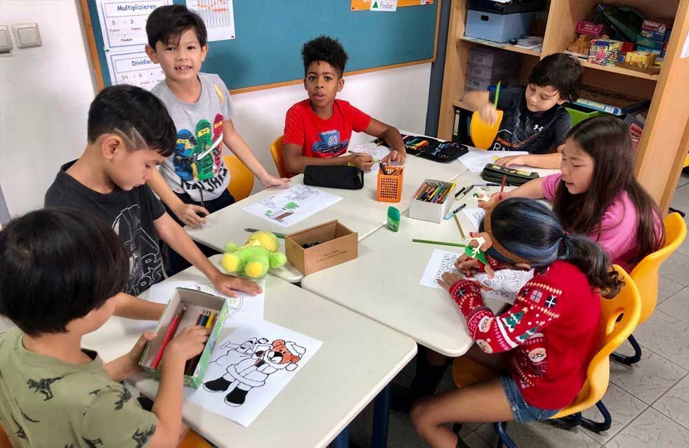 A group of children are sitting around a table in a classroom.