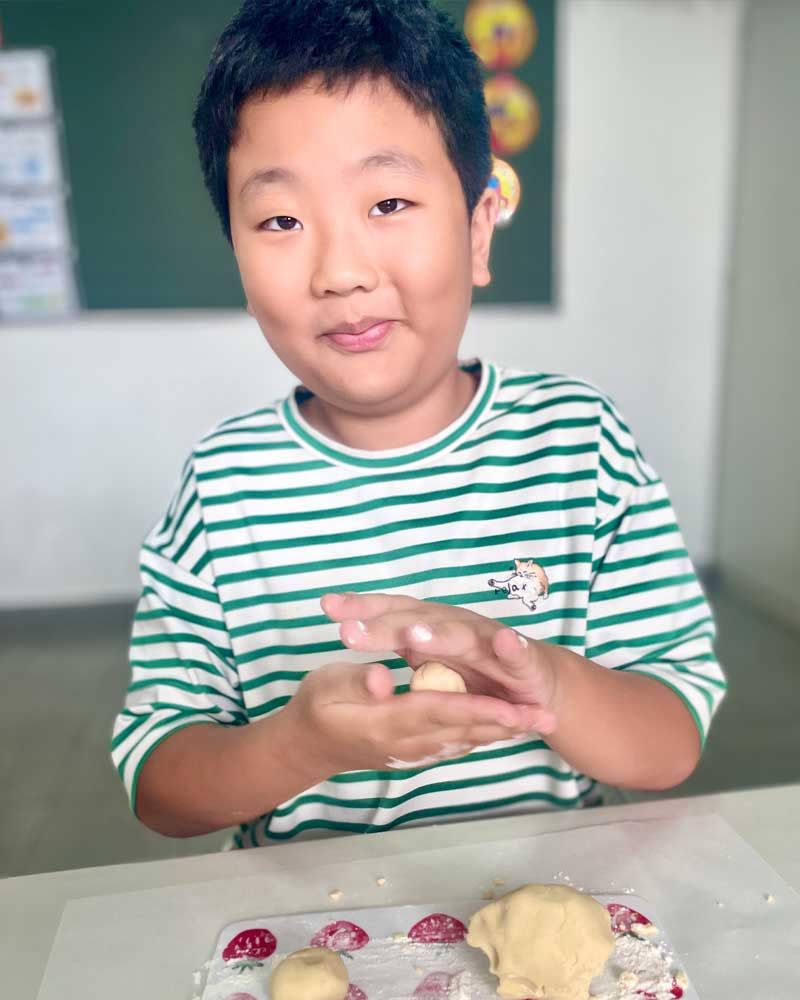 A young boy is sitting at a table with dough in his hands.