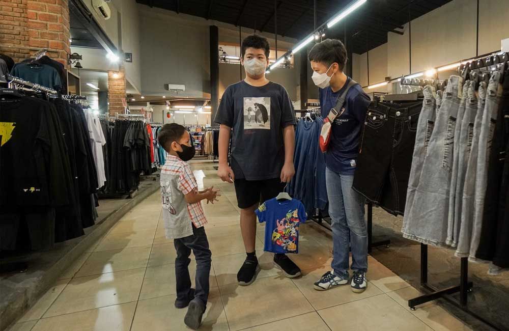 Three young boys wearing face masks are standing in a clothing store.