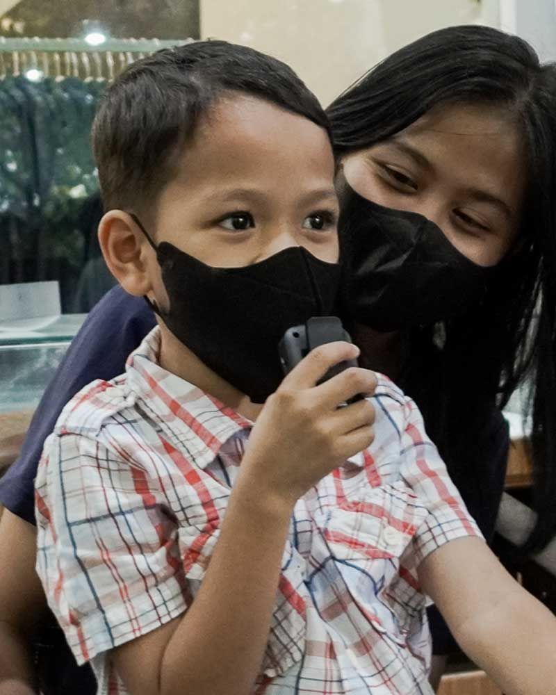 A little boy wearing a mask is holding a cell phone