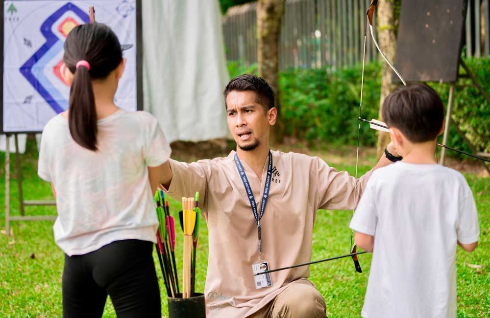 A man is teaching two children how to archery.