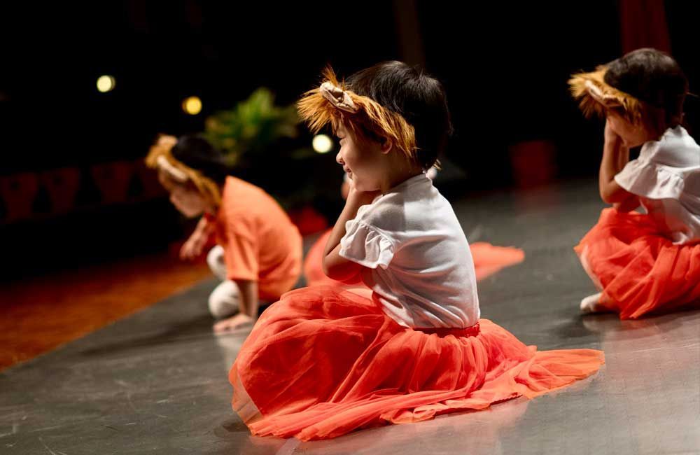 A group of young girls are sitting on the floor on a stage.