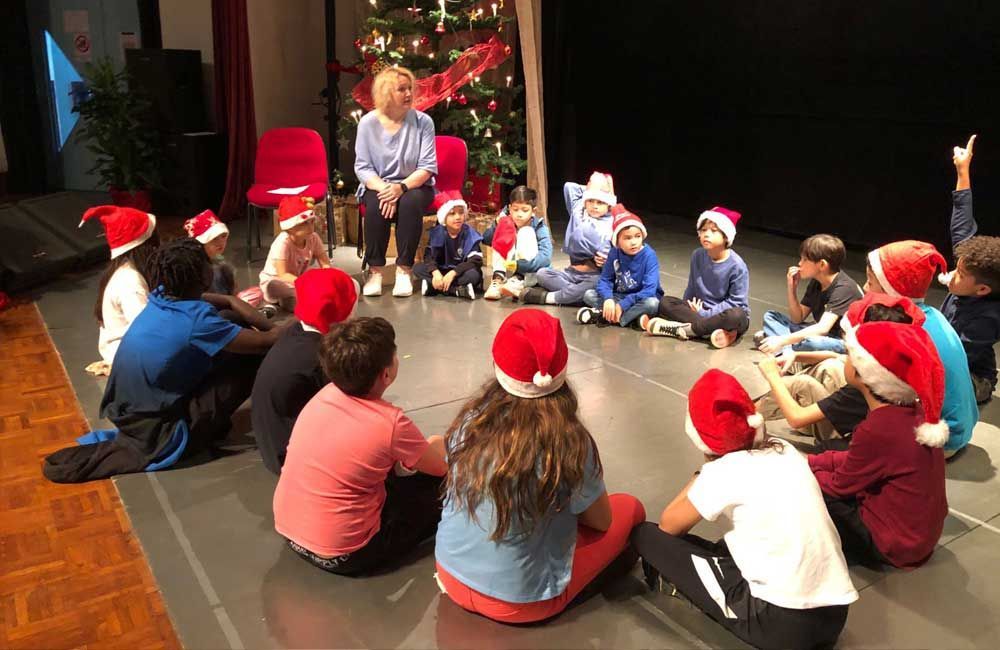 A group of children wearing santa hats are sitting in a circle on the floor.