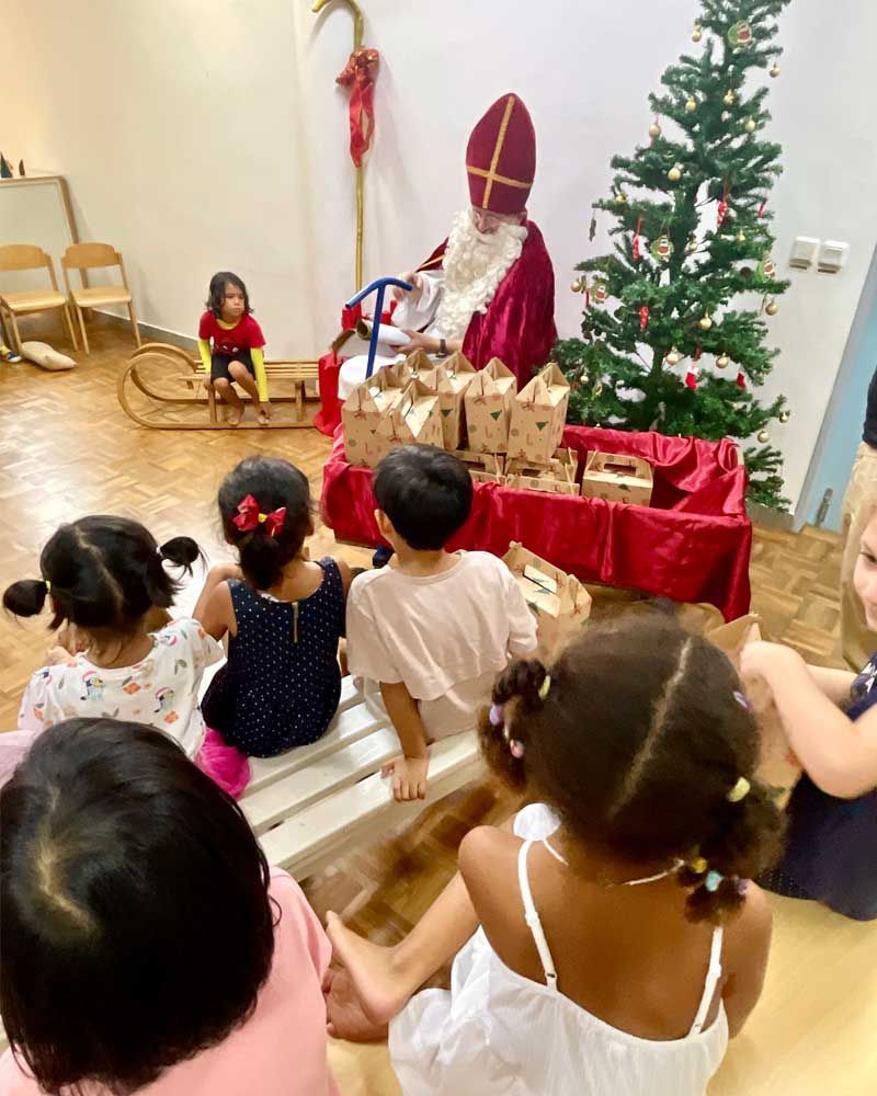 A group of children are sitting on a bench in front of a christmas tree.