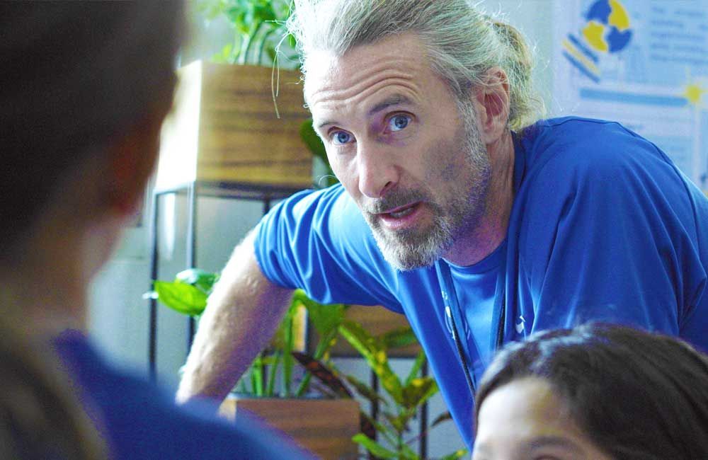 A man in a blue shirt is talking to a group of people.