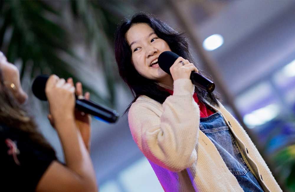 A woman is singing into a microphone while another woman looks on.