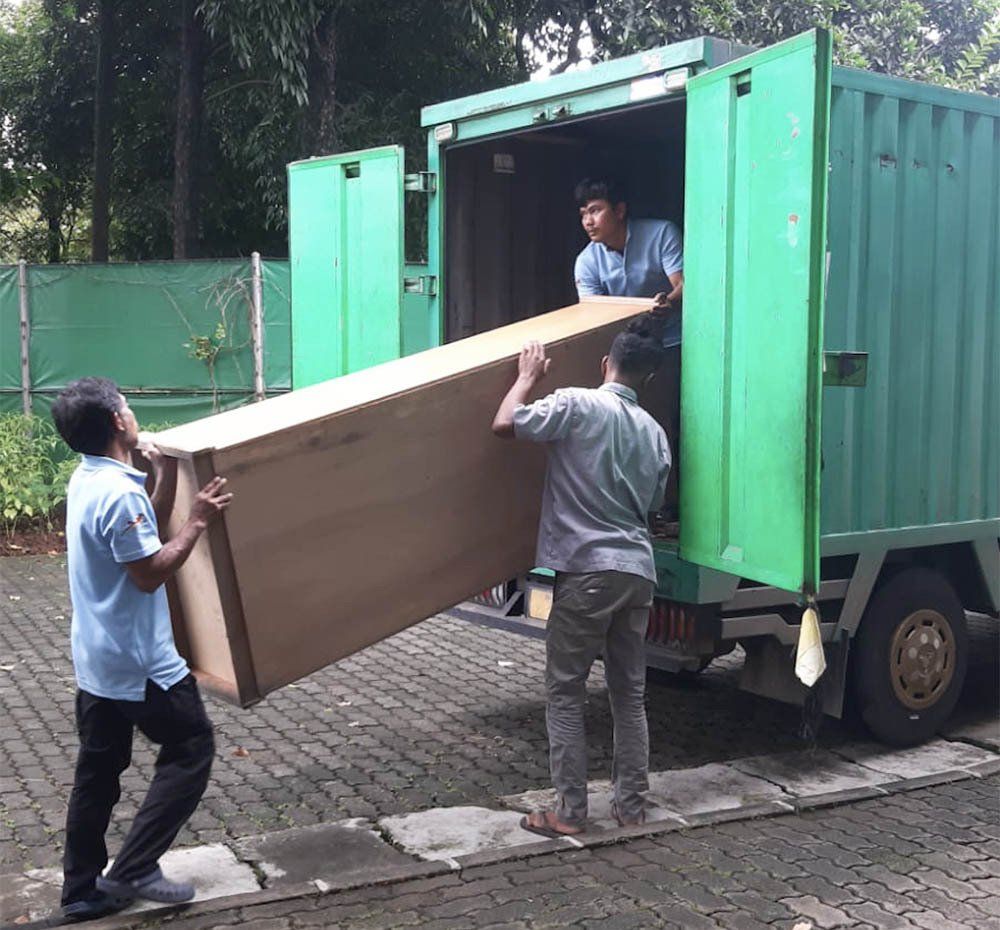 Two men are carrying a large piece of wood into a green truck