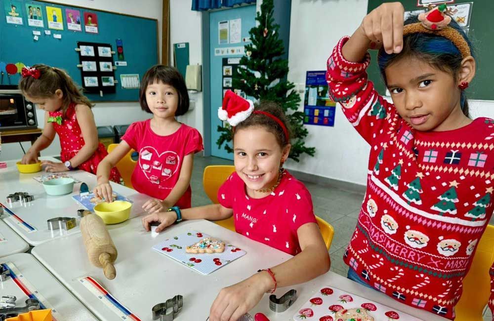 A group of young girls are sitting at a table making christmas cookies.