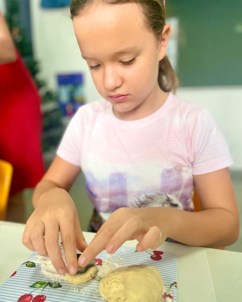 A little girl is sitting at a table making dough.