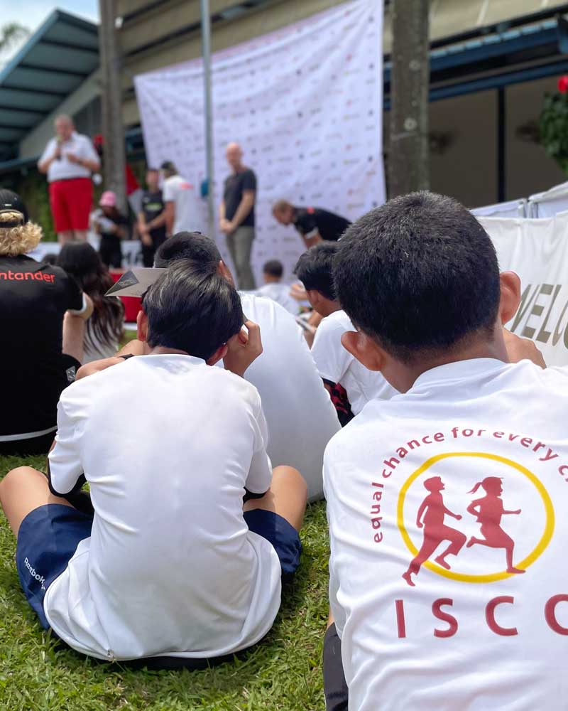 A group of people are sitting on the grass watching a presentation.