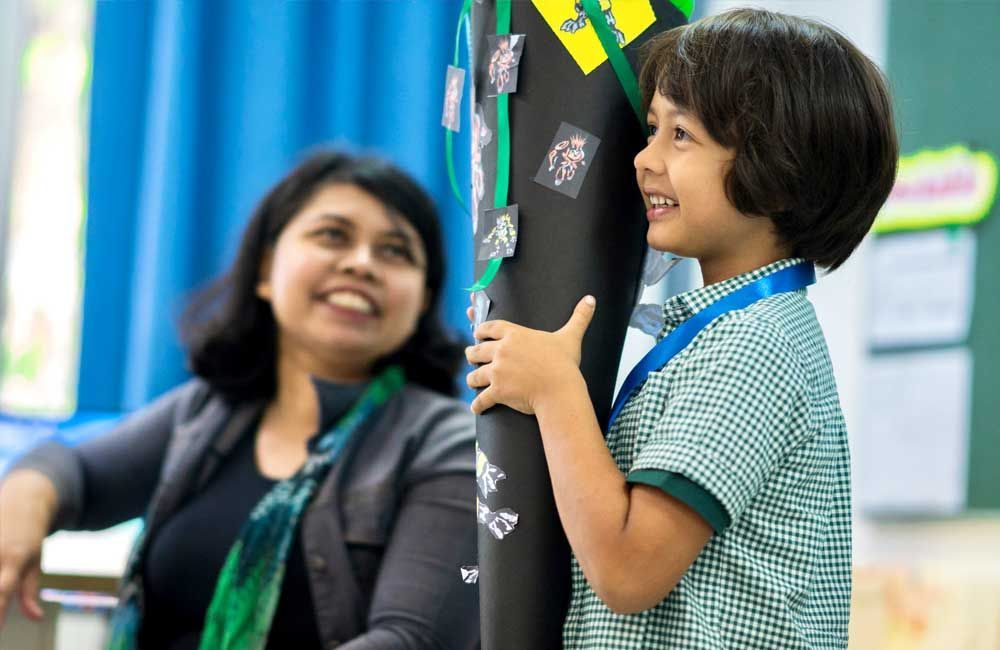 A woman is sitting next to a young boy holding a cone in a classroom.