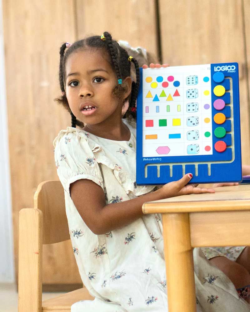 A little girl is sitting at a table holding a puzzle.