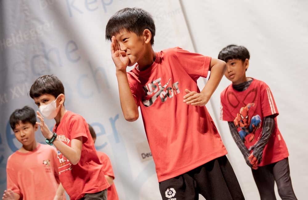 A group of young boys wearing red shirts are dancing on a stage.