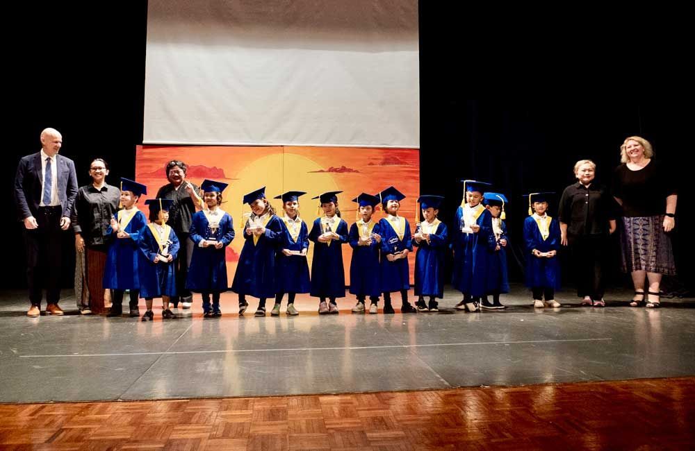 A group of children in graduation caps and gowns are standing on a stage.