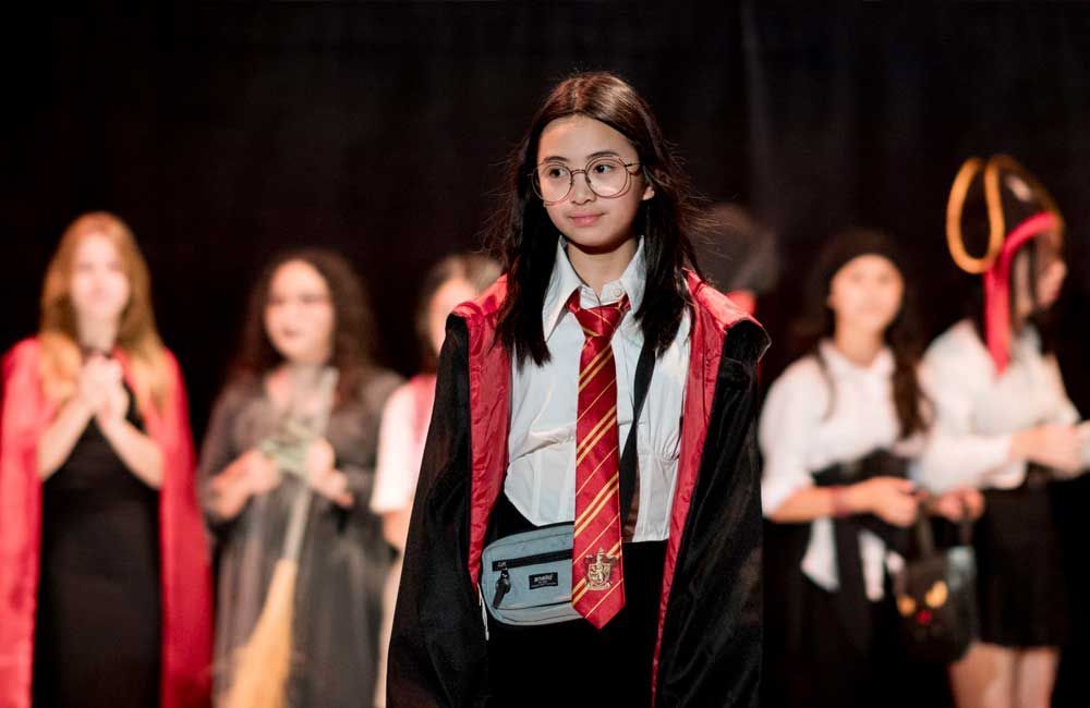 A girl in a harry potter costume is standing in front of a group of people.
