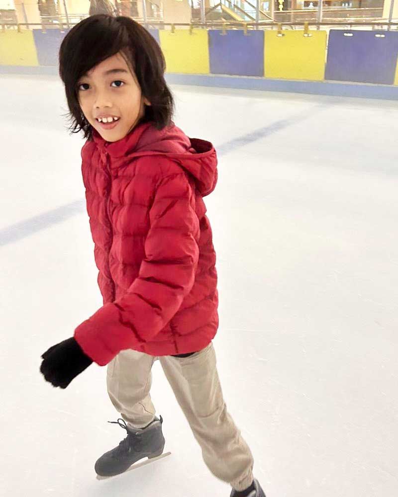 A young boy in a red jacket is ice skating