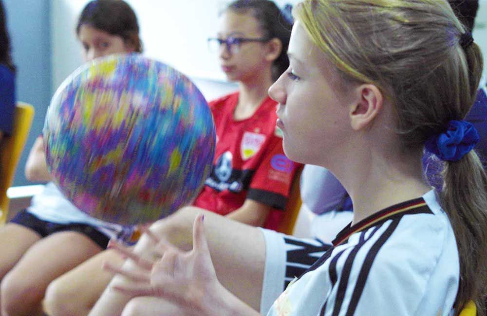 A girl is sitting in a classroom holding a colorful ball.