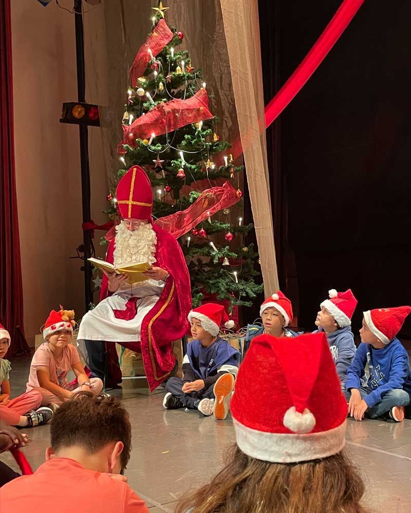 A man dressed as santa claus is reading a book to children in front of a christmas tree.