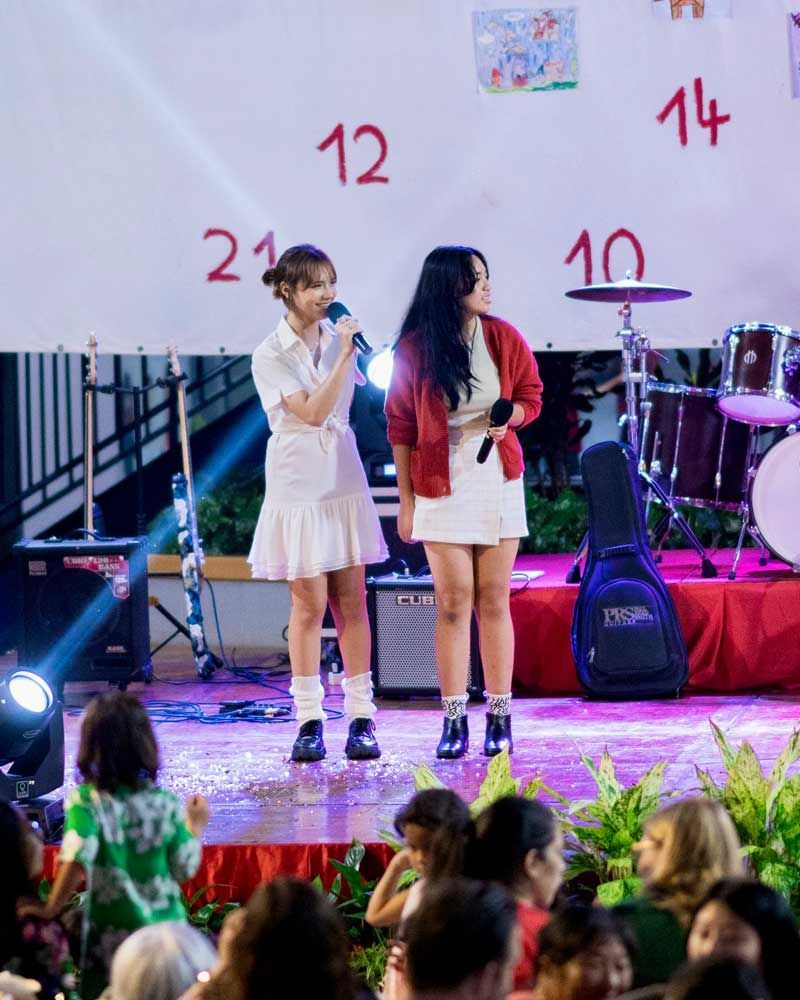 Two women are singing into microphones on a stage in front of a crowd.