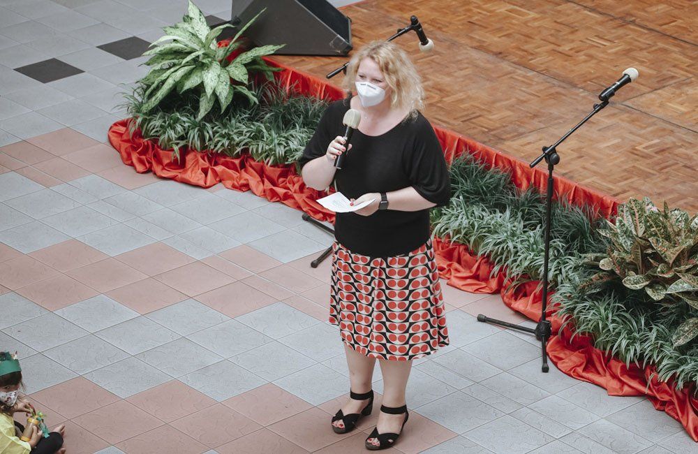 A woman wearing a mask is standing on a stage holding a microphone.