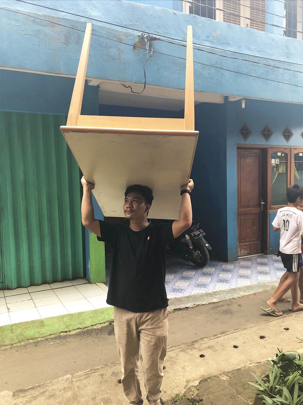 A man is carrying a wooden chair on his head.