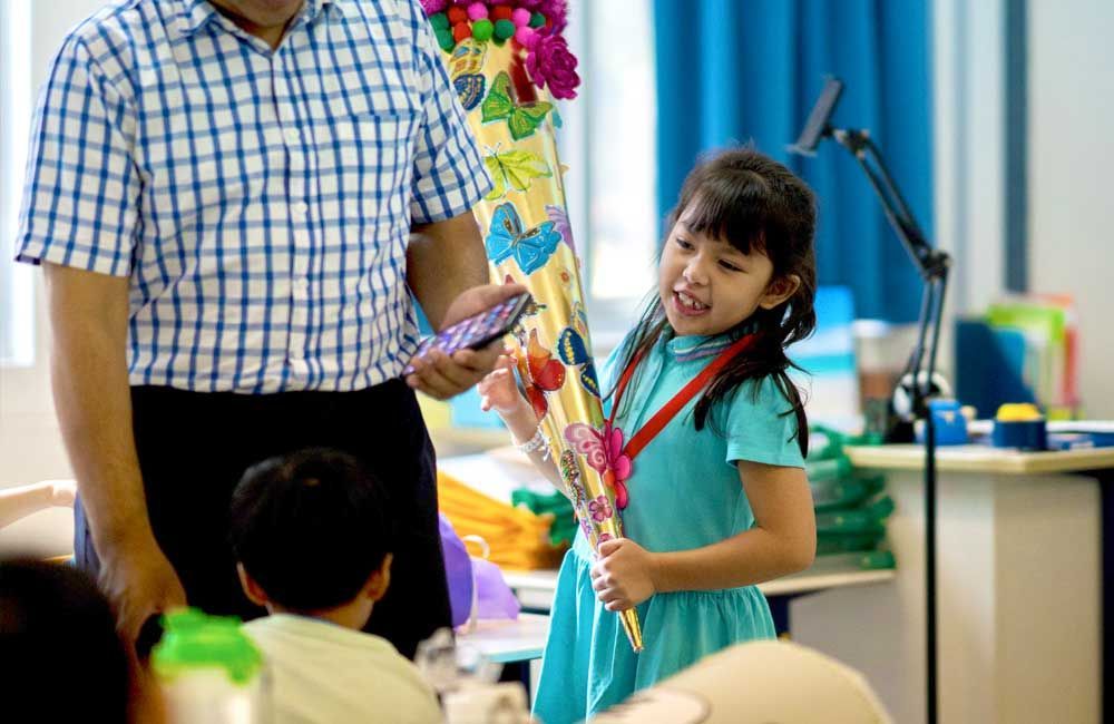 A little girl is holding a bouquet of flowers while standing next to a man in a classroom.