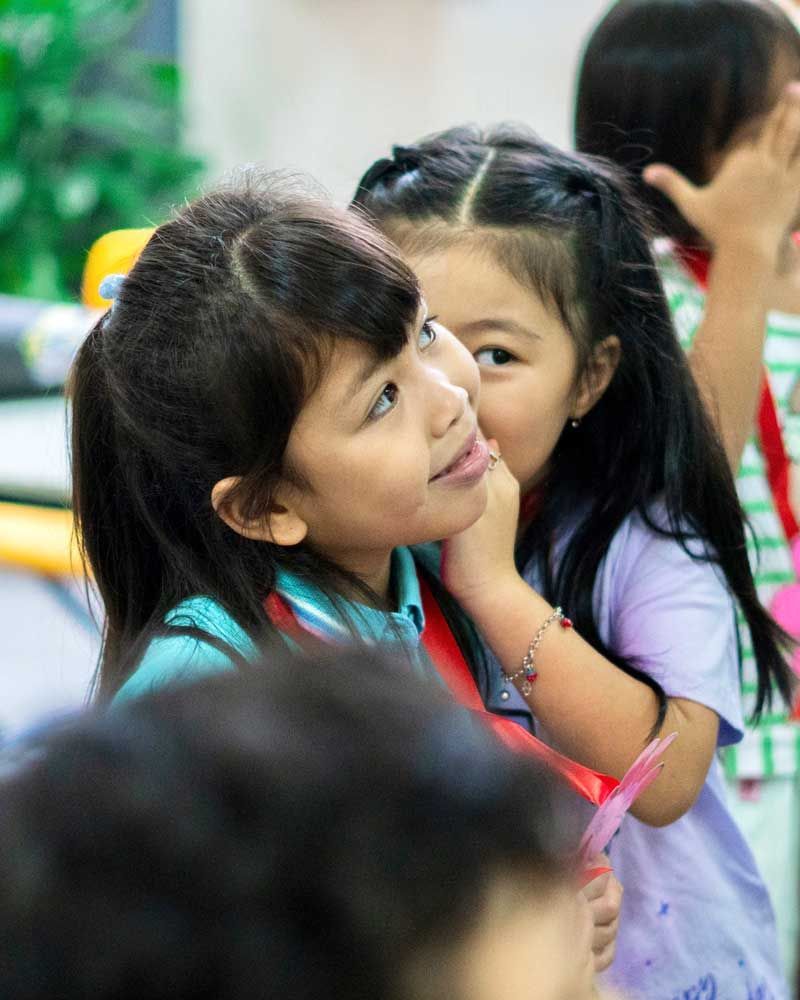 Two little girls are sitting next to each other in a classroom.