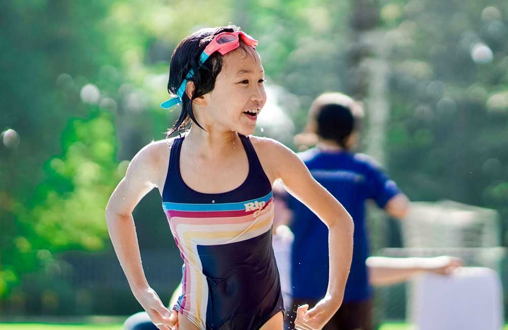 A young girl in a swimsuit and goggles is running in the water.