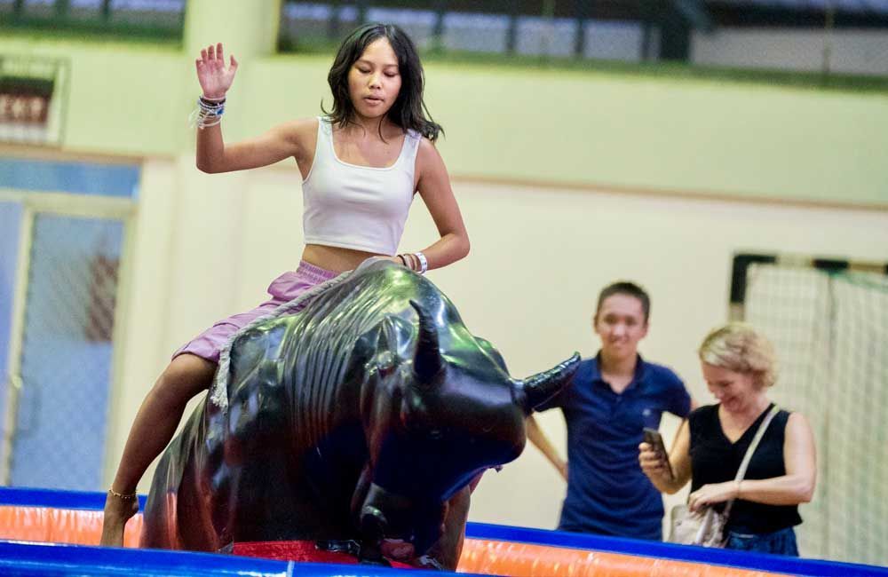 A woman is riding a mechanical bull in a gym.