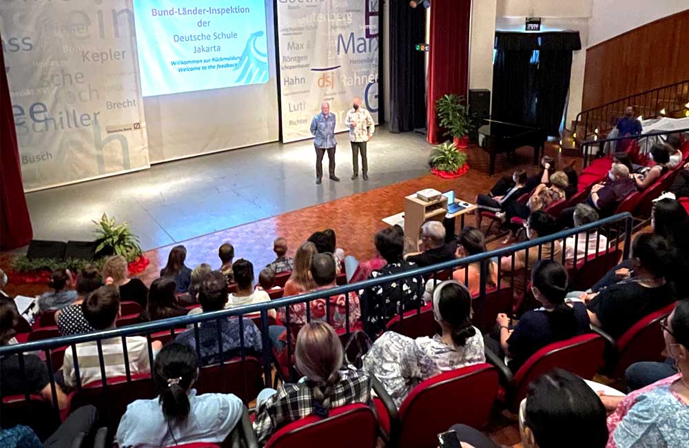A group of people are sitting in an auditorium watching a presentation on a stage.