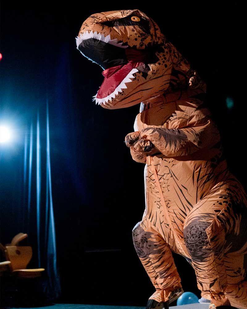 A person in an inflatable dinosaur costume is standing on a stage.
