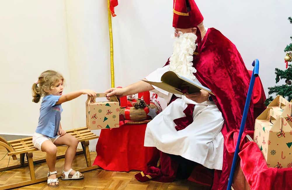 A little girl is sitting on a sled next to a man dressed as santa claus.