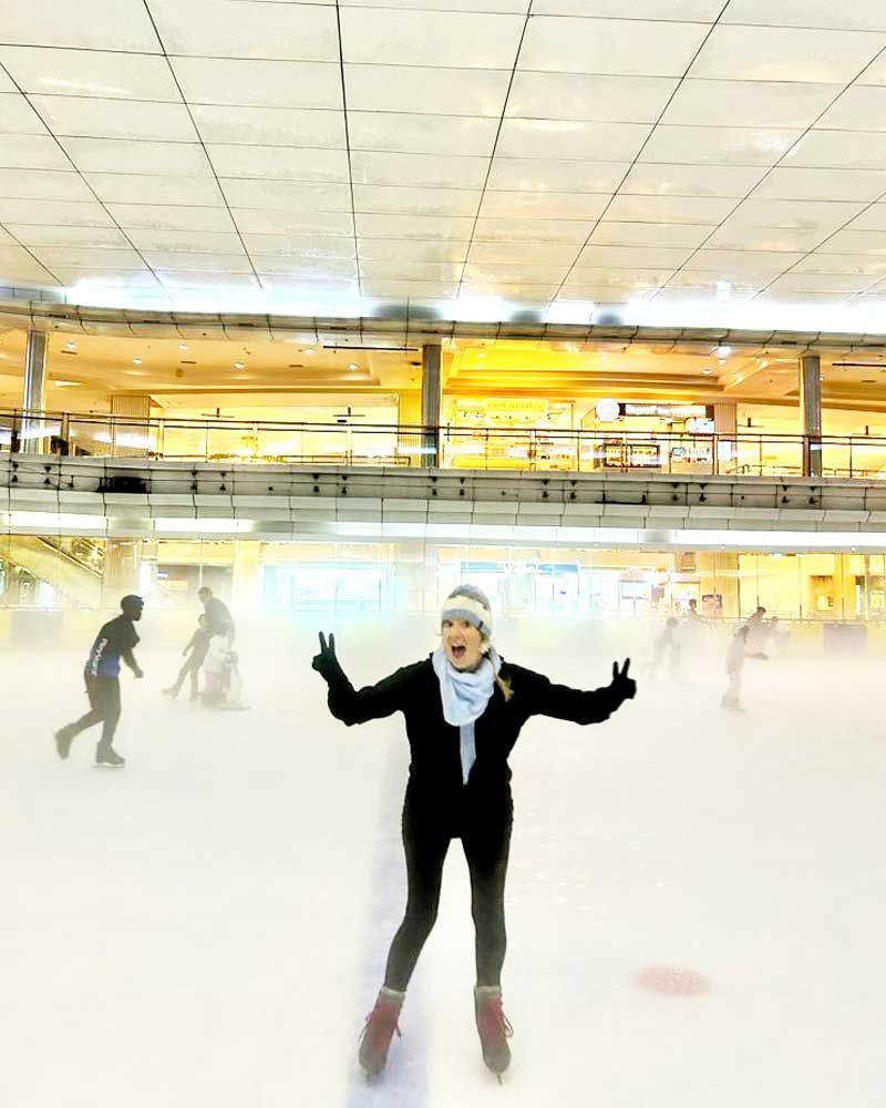 A woman is standing on a ice rink with her arms outstretched.