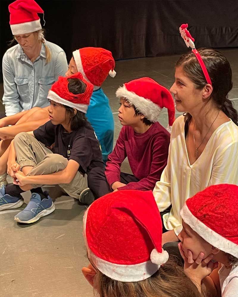 A group of children wearing santa hats are sitting on the floor.