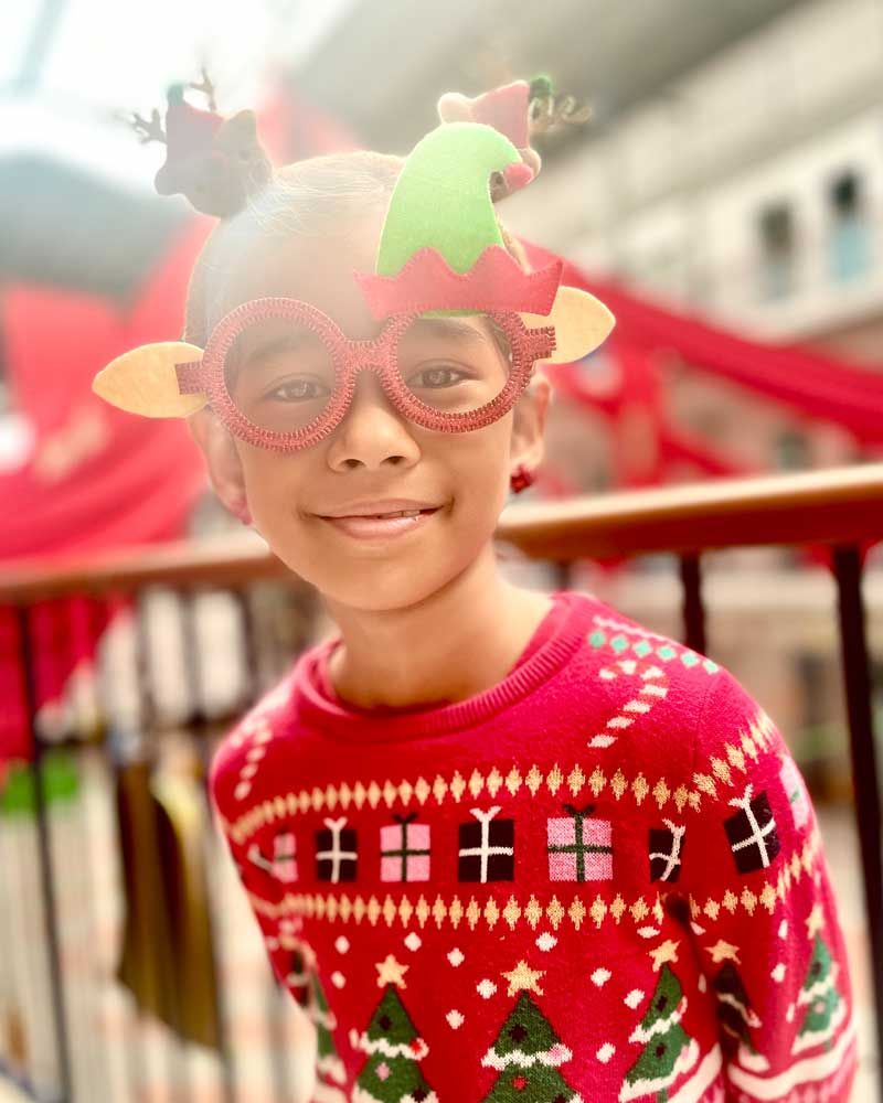A young boy wearing a christmas sweater and glasses