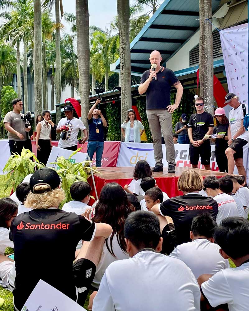 A man is standing on a stage talking to a crowd of people.