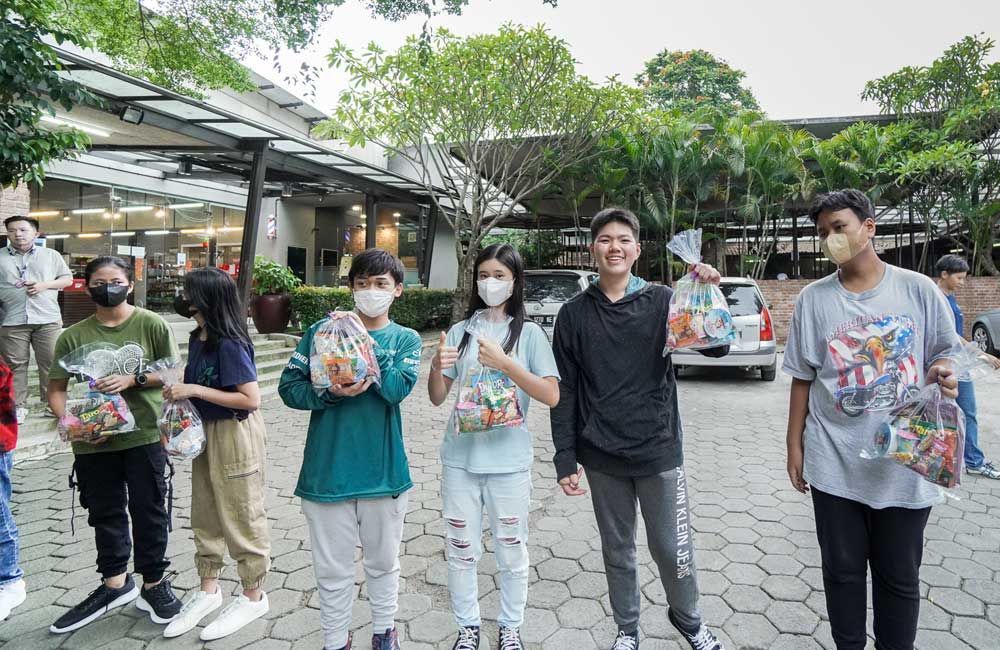 A group of young people wearing face masks are standing next to each other holding bags of candy.