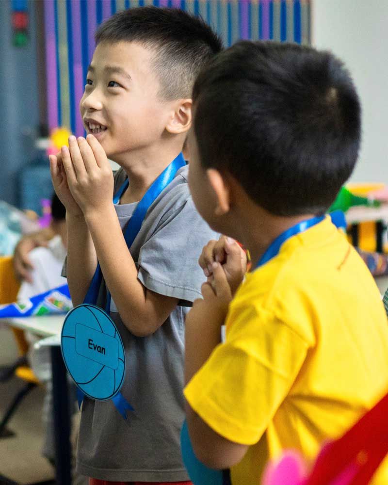 Two young boys wearing medals in a classroom.