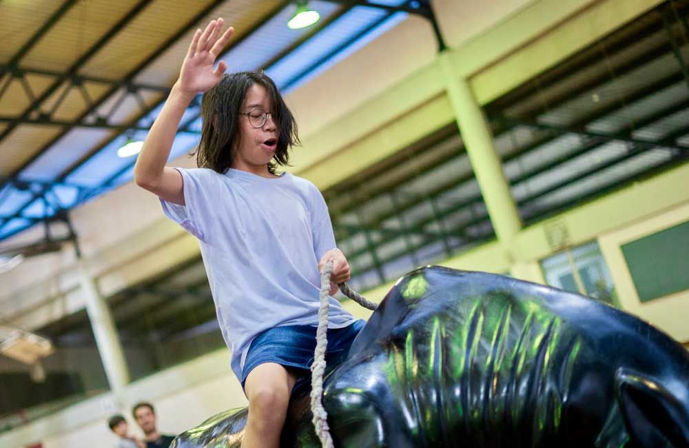 A young girl is riding a mechanical bull in a gym.