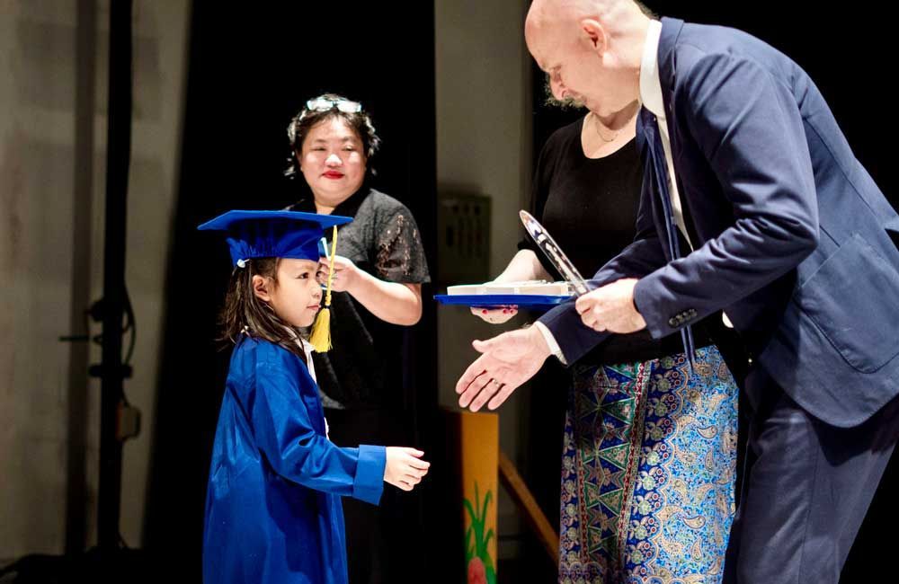 A man in a suit is shaking hands with a little girl in a graduation cap and gown.