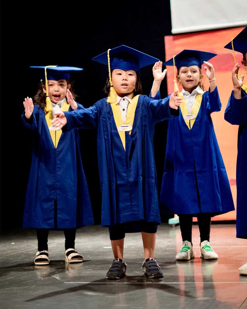 A group of children wearing graduation caps and gowns are standing on a stage.