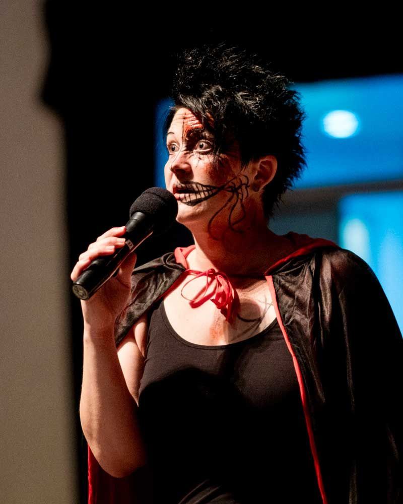 A woman in a vampire costume is singing into a microphone