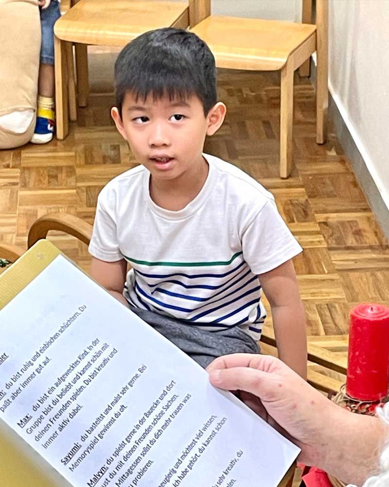 A young boy is sitting on a bench while a person holds a piece of paper in front of him.